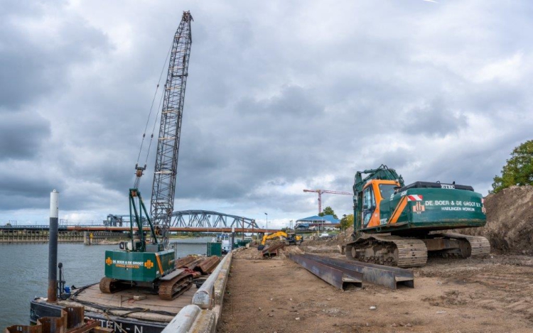 De machine die de damwanden de grond intrilt, op een ponton.